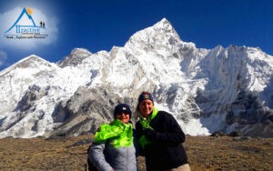 Two smiling female trekkers in warm jackets posing in front of snow-capped Mount Ama Dablam in Nepal.